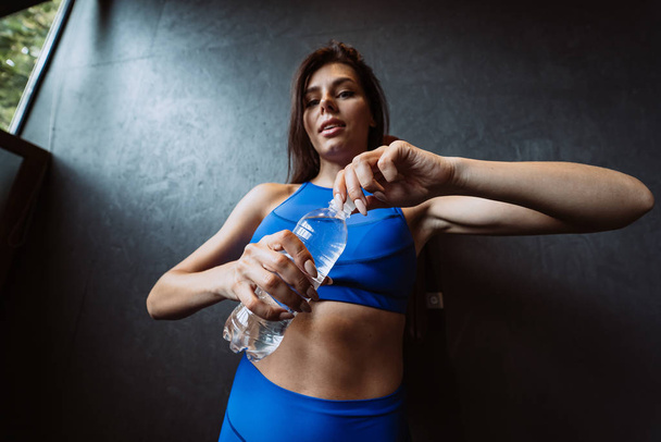 Fit woman posing on the camera. Girl opens a water bottle. Beauty of modern sport. - Foto, Imagem