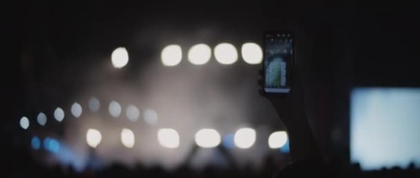 Henkilö ottaa valokuvan konsertin aikana, taustalla välkkyvät valonheittimet. Ihmiset suoran esityksen näyttämöllä yökerhossa. Keskikokoinen, ampumisen takana, kädessä pidettävä, hidastettuna. BMPCC 4K
  - Materiaali, video