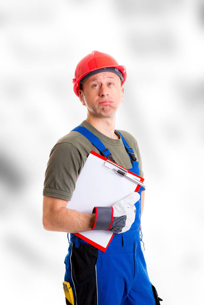 young workman in blue dungarees with clipboard looking sceptical - Photo, image