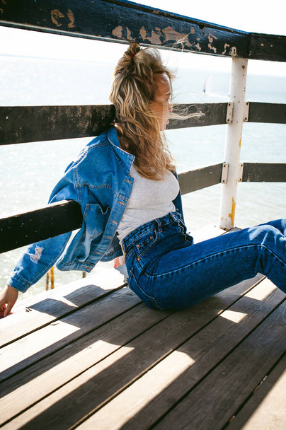 young beautiful woman in jeans clothes outdoors. portrait of a girl with freckles on her face, stylish girl on sea beach rescue tower, on a sunny summer autumn day. - 写真・画像