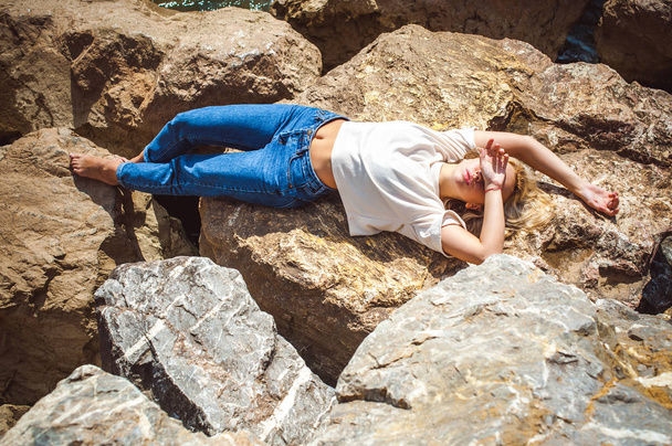 Portrait young woman on stones near sea. Beautiful girl is resting on coast, enjoying outdoor recreation. - Foto, Imagen