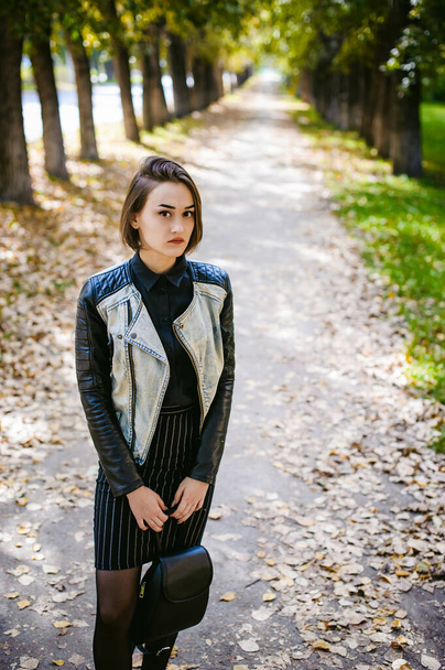 street portrait of a girl student, fashionably dressed in dark clothes, with a black backpack and denim jacket autumn sunny day - Фото, зображення