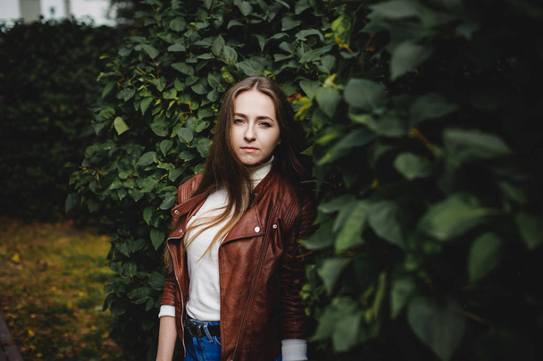 street portrait of a female student in fashionable clothes, blue jeans and a brown jacket, outdoors - Photo, Image