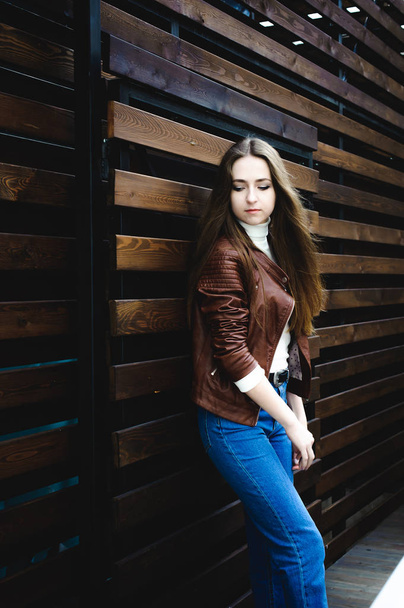 street portrait of a female student in fashionable clothes, blue jeans and a brown jacket, outdoors - Fotó, kép