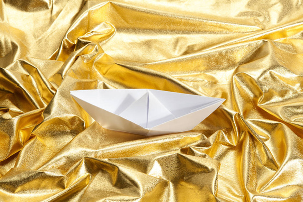 a paper origami boat sailing in a gold fabric choppy waters. Luxury composition. Minimal color still life photography. - Zdjęcie, obraz