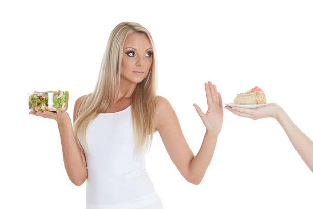 Young beautiful woman choosing between bowl of salad with fresh vegetables and piece of cake on a white background.  Concept of healthy food. - Foto, afbeelding