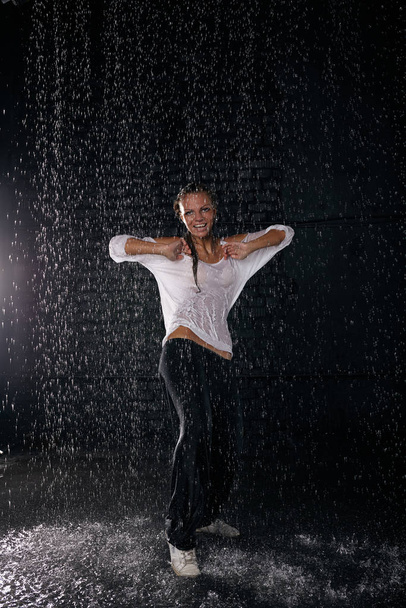 The beautiful girl dancing in water under rain on a black background.  Modern dances. - Φωτογραφία, εικόνα