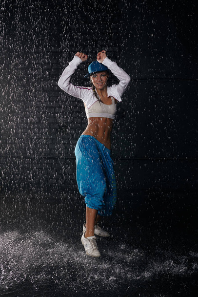 The beautiful girl dancing in water under rain on a black background.  Modern dances. - Valokuva, kuva