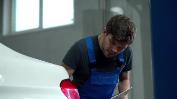Mecánico inspecciona los faros de un coche y escribe algo
  - Imágenes, Vídeo