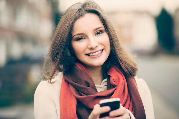 Happy with mobile. Businesswoman with phone outdoors smiling looking at you camera cellphone in hands isolated unfocused  street background in city of Brussels Belgium  - Photo, image