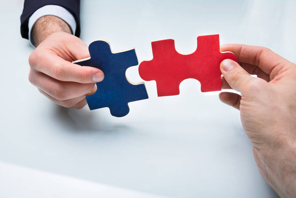 Close-up Of Two Businesspeople Holding Red And Blue Jigsaw Puzzle - Valokuva, kuva