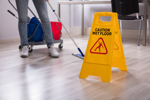 Close-up Of Yellow Wet Floor Caution Sign Near Janitor Cleaning Office - Foto, afbeelding