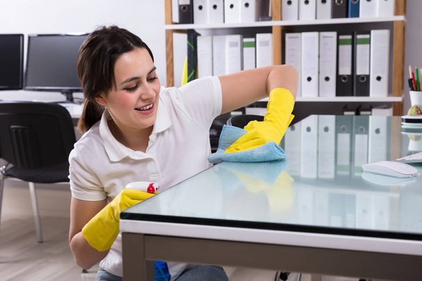 Close-up Of A Smiling Young Woman Cleaning The Glass Office Desk With Rag In Office - Foto, afbeelding