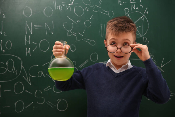Schoolboy holding flask near chalkboard with chemical formulas - 写真・画像