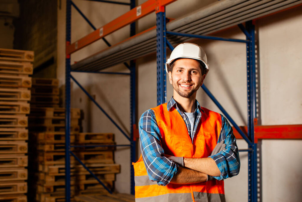 Confident handsome worker in protective hardhat and uniform at the warehouse of a industrial manufacturing - Photo, Image