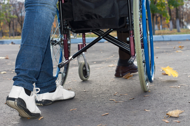 τα πόδια του ένα φροντιστή που ωθούν μια αναπηρική καρέκλα - Φωτογραφία, εικόνα