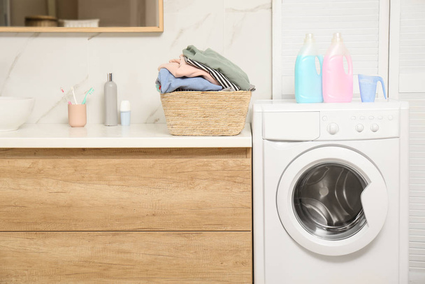 Wicker basket with laundry, detergents and washing machine in bathroom - Фото, изображение