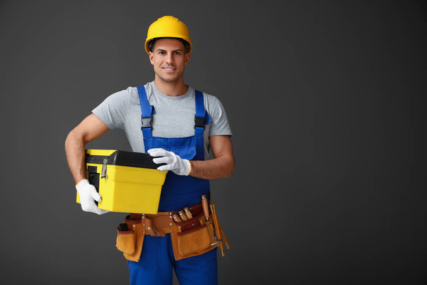 Handsome carpenter with tool box on dark background. Space for t - Zdjęcie, obraz