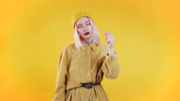 Beautiful woman with pink hair and piercing dancing and snaps fingers on colorful yellow studio background. Cute girls portrait. Party, happiness, freedom, youth concept. - Video