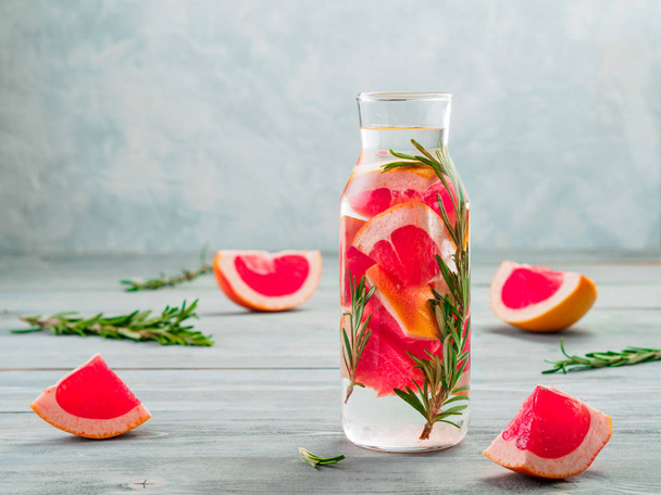infused detox water with grapefruit and rosemary in glass bottle on gray wooden table. diet healthy eating and weight loss concept, copy space for text - Фото, изображение