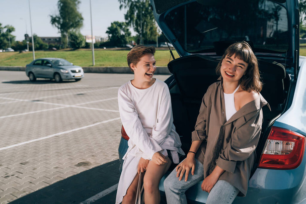 Deux filles dans le parking au coffre ouvert posant pour la caméra. - Photo, image