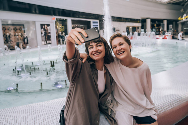 Deux filles prennent un selfie dans le centre commercial, une fontaine en arrière-plan
 - Photo, image