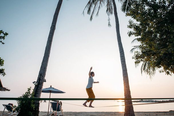 Dziewczyna idzie na slackline o zachodzie słońca na tropikalnej plaży - Zdjęcie, obraz