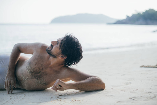 Красивый мужчина лежит на песке у океана
.  - Фото, изображение