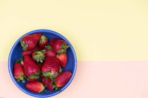 Erdbeeren in blauer Schale auf pastellorangefarbenem und gelbem Grund von oben - Foto, Bild