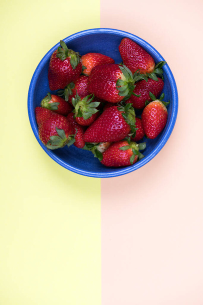strawberries in blue bowl on pastel orange and yellow ground from above - Фото, изображение