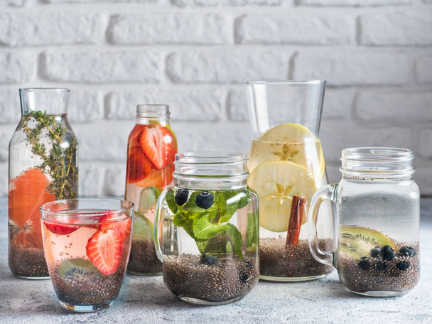 Different chia water in glass on gray background. Chia infused detox water with berries, fruits and herbs. Healthy eating, drinks, diet, detox concept. Copy space for text - Foto, immagini