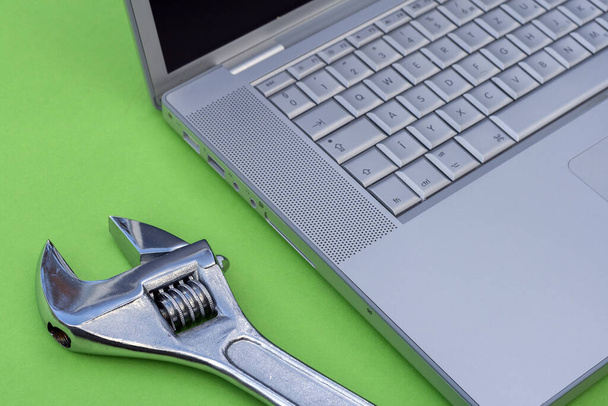 Nastavitelný klíč vedle stříbrného laptopu. Počítačový servis, motiv údržby. - Fotografie, Obrázek