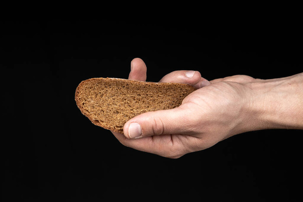 Homem segura um pedaço de pão na mão sobre fundo preto
 - Foto, Imagem