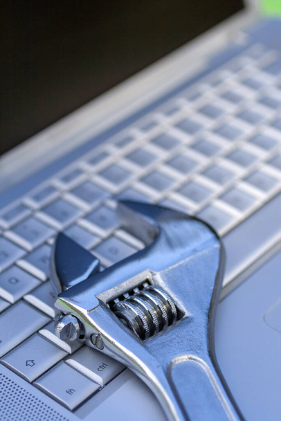 Adjustable wrench next to a silver laptop. Computer service, maintenance theme. - Photo, Image