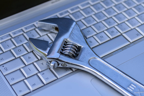 Регулируемый гаечный ключ рядом с серебряным ноутбуком. Компьютерный сервис, тема обслуживания
. - Фото, изображение