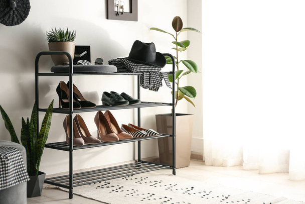 Black shelving unit with shoes and different accessories near white wall in hall - Zdjęcie, obraz