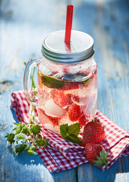Fresh, chilled fruit and berry infused punch in a glass jar with a straw on a bright outdoor table setting. - Foto, Imagen