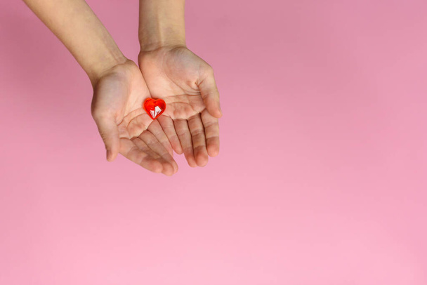 Руки, дающие красное сердце на розовом фоне. День святого Валентина
. - Фото, изображение