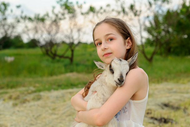 girl with baby goat on farm outdoors. Village animals. happy child hugs goat, concept of unity of nature and man. - Photo, Image