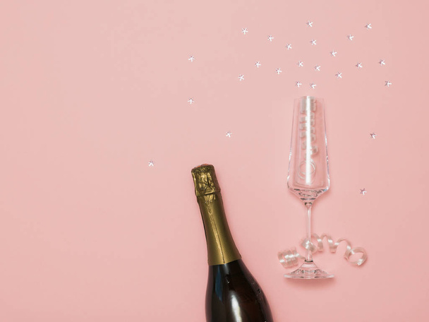A bottle of sparkling wine and a glass with streamers and stars on a pink background. - Foto, Imagen