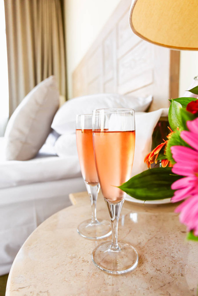 Two glasses of rose champagne in the upscale hotel room. Dating, romance, honeymoon, valentine, getaway, staycation, digital detox concepts - Photo, Image