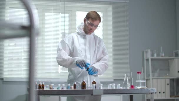 Mies suojaavissa työvaatteissa ja käsineissä työskentelee kemiallisten laitteiden kanssa laboratoriossa
 - Materiaali, video