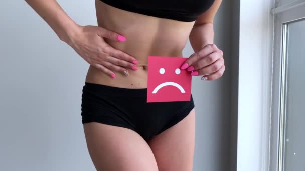 Υγεία της γυναίκας. Γυναικείο σώμα κρατά θλιμμένο εικονίδιο κάρτα κοντά στο στομάχι - Πλάνα, βίντεο
