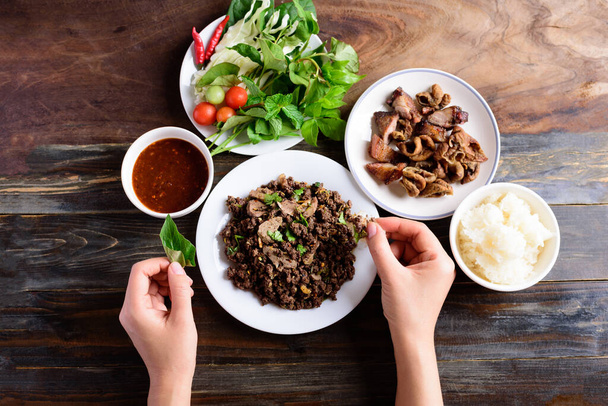 Severní thajské jídlo, pikantní mletý vepřový salát (Larb Moo Kua) s lepkavou rýží, grilovaným střevem a čerstvou zeleninou na dřevěném pozadí, výhled shora - Fotografie, Obrázek