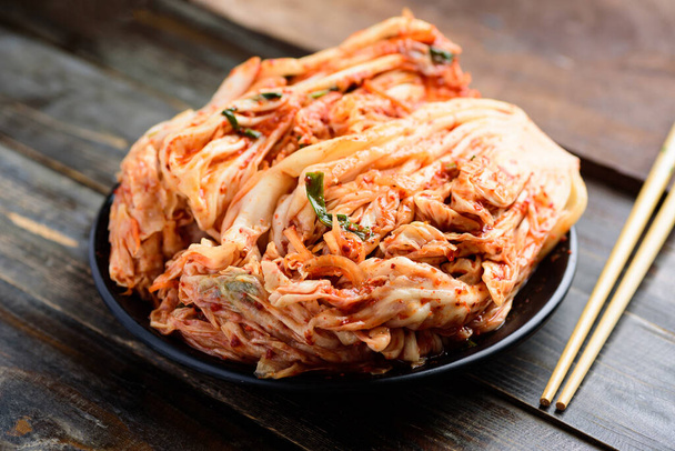 Kimchi Kohl auf schwarzem Teller und Essstäbchen auf hölzernem Hintergrund - Foto, Bild