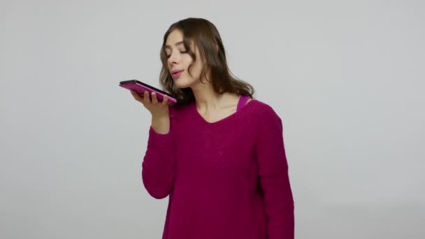 Brunette woman in pullover making voice records on mobile phone, talking to smart device giving command - Filmagem, Vídeo