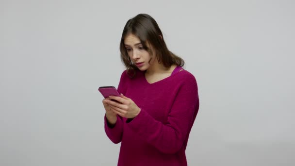 Young positive pretty woman in pullover using mobile phone, expressing amazement and shock after reading message - Séquence, vidéo
