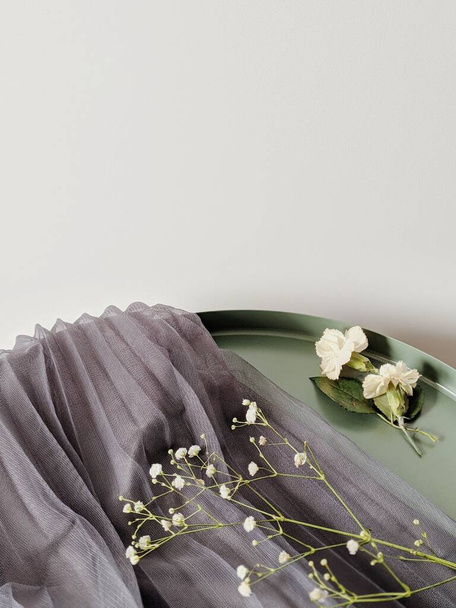 Minimális összetétel szárított ággal és két bimbó virággal egy szürke textilen és zöld asztalon. Tavaszi koncepció. Másold a helyet. Trendi tervezés. - Fotó, kép