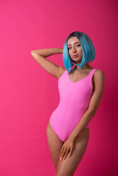 Pretty woman in a pink monokini and blue wig in the studio. Girl with artificial short hair posing in a colored swimsuit. - Zdjęcie, obraz