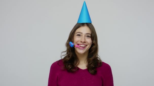 Humorous happy brunette woman with funny cone on head blowing party horn, congratulating on birthday anniversary - Πλάνα, βίντεο